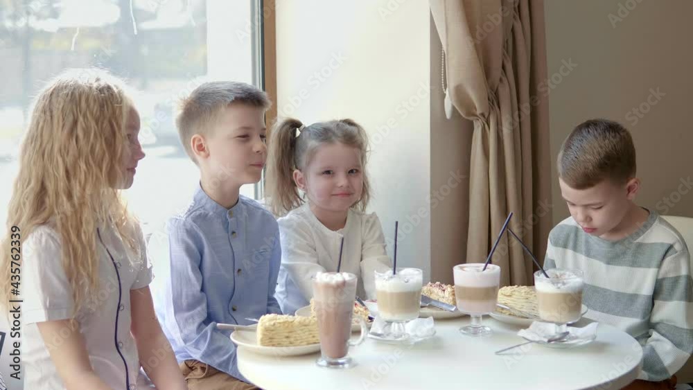 A group of children are sitting in a cafe without their parents and celebrating with dessert. Boys and girls get ready to enjoy dessert in the cafe A group of children are sitting in a cafe without their parents and celebrating with dessert. Boys and girls get ready to enjoy dessert in the cafe