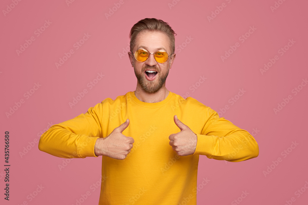 Cheerful man in yellow glasses showing thumbs up