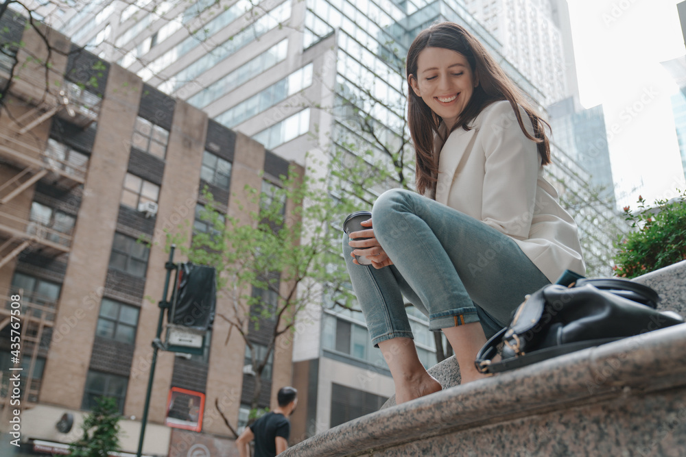 Smiling positive young woman relaxing having a break, city streets. Stylish fashion blogger concept, long brown hair, blazer, blue jeans, leather bag. New York modern buildings background Smiling positive young woman relaxing having a break, city streets. Stylish fashion blogger concept, long brown hair, blazer, blue jeans, leather bag. New York modern buildings background