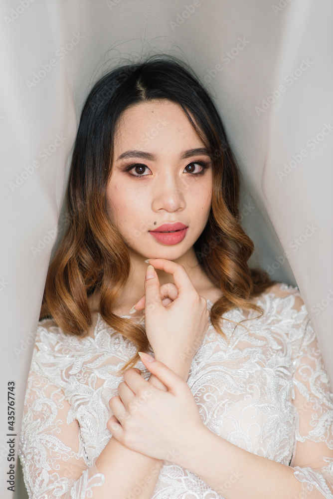 Asian bride in wedding dress in hotel sitting on the bed, standing near window, morning Asian bride in wedding dress in hotel sitting on the bed, standing near window, morning