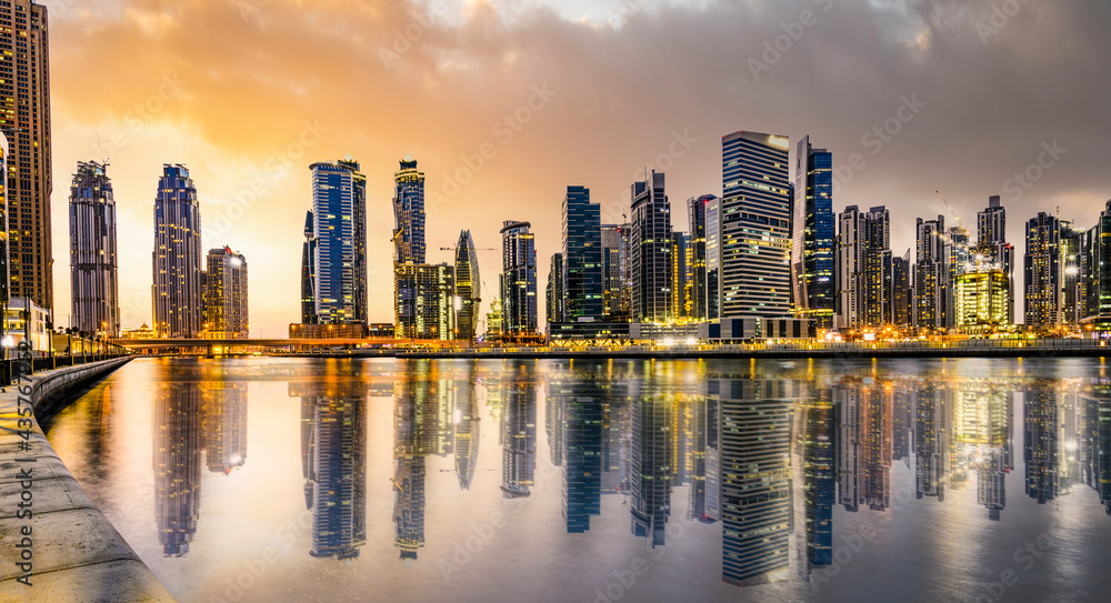 Stunning view of the illuminated Dubai skyline during a dramatic sunset. Buildings and skyscrapers reflected on a silky smooth water flowing in the foreground. Dubai, United Arab Emirates.