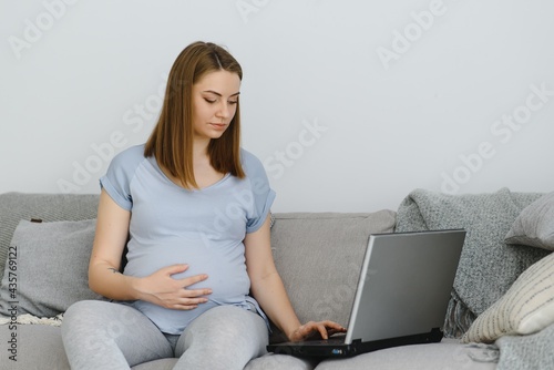 side view of pregnant freelancer sitting on sofa near laptop