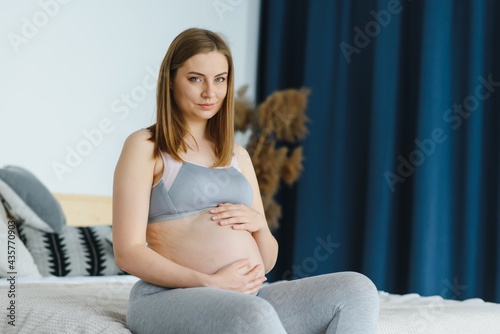 Attractive pregnant woman is sitting in bed and holding her belly. Last months of pregnancy. Pregnant Young Girl. Healthcare Concept. Healthy Food Concepts. Relaxing at Home. Care of Pregnant.