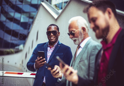 Three business men in the city standing on street and using mobile phones. Focus is on background.