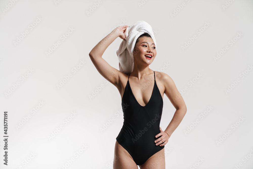 Fototapeta premium Brunette asian woman wearing swimsuit and towel smiling at camera