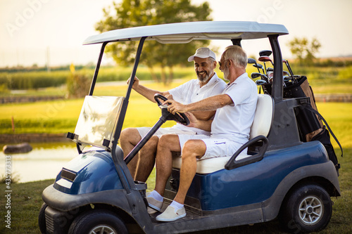Two older friends are riding in a golf cart. photo