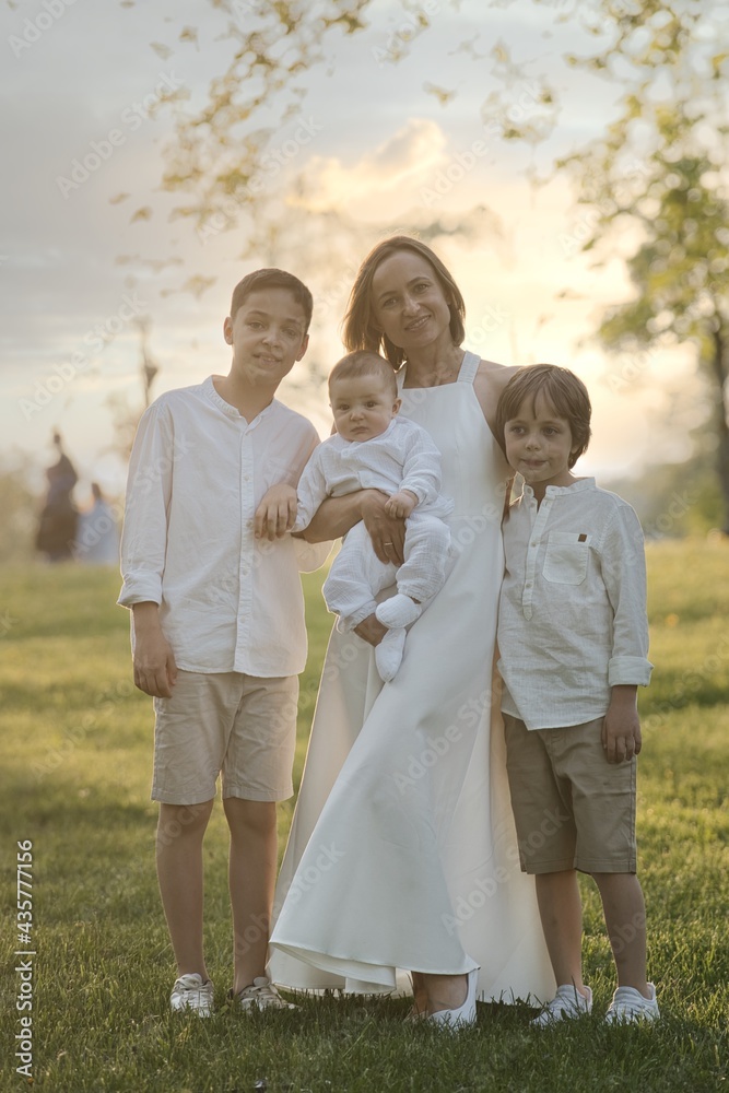 Mother and three children hugging. Happy family sitting outdoor: woman and two brother kids boys and cute little toddler boy Mother and three children hugging. Happy family sitting outdoor: woman and two brother kids boys and cute little toddler boy