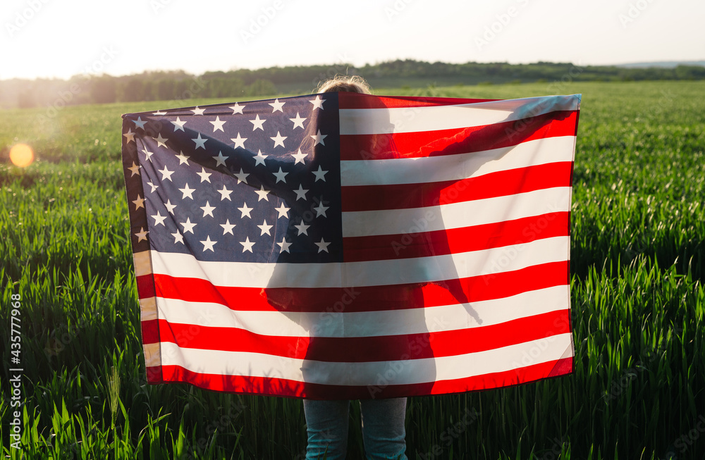Naklejka premium Happy young woman holding American flag at sunset. 4th of July. Independence Day.