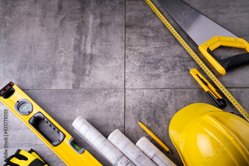 Contractor theme. Tool kit of the contractor: yellow hardhat, libella and tools on the gray tiles background. © zolnierek