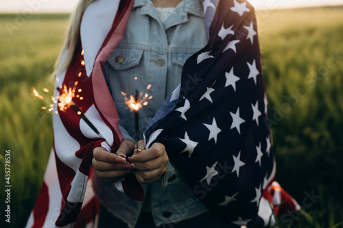 Young girl holding bengal fire with American flag at sunset. America celebrate 4th of July. Independence Day. © Miha Creative