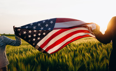 Patriotic holiday. Young patriotic couple with the American flag in a wheat field at sunset. Independence Day, 4th of July.	