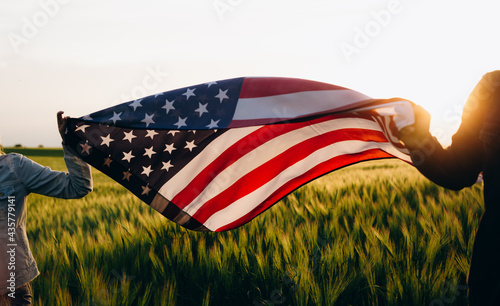 Patriotic holiday. Young patriotic couple with the American flag in a wheat field at sunset. Independence Day, 4th of July.	