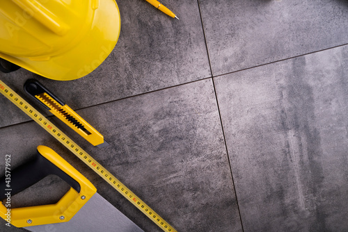 Contractor theme. Tool kit of the contractor: yellow hardhat, libella and tools on the gray tiles background.