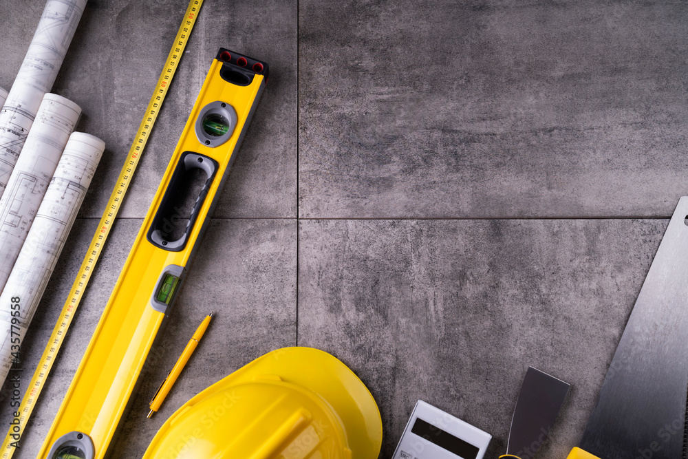 Contractor theme. Tool kit of the contractor: yellow hardhat, libella and tools on the gray tiles background.