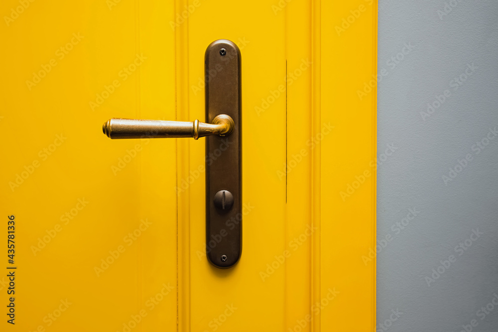Yellow door with a bronze door handle close-up. - obrazy, fototapety, plakaty 