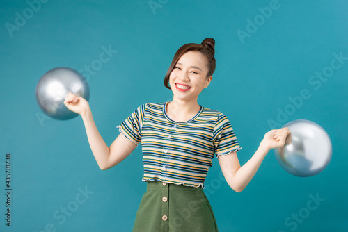 Young happy woman holding silver balloons on blue background