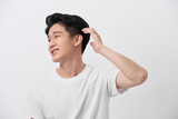 Confident smiling handsome young man in white t shirt. standing on the pure background, fixing his perfect hairstyle