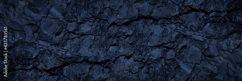 Black blue stone background. Toned rock texture. Wide banner. Dark grunge background with copy space for design. Cracked granite surface. Close-up.