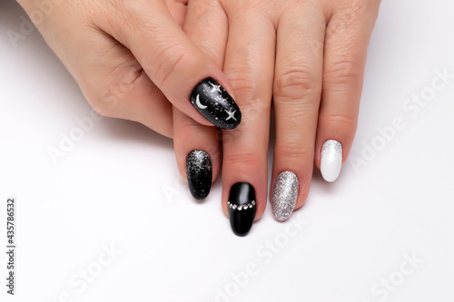 Black, white, silver manicure with crystals, painted stars and the moon on long oval nails close-up on a white background. Festive manicure.