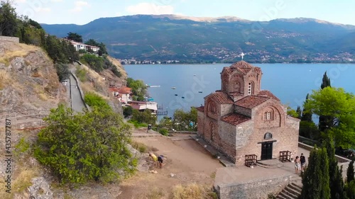 An gothic old orthodox church at coast of lake Ohrid. Beautiful medieval architecture, forest and emerald colored water. Aerial drone footage took with 4K 30fps.