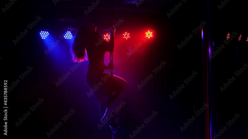 A flexible dancer dances on a pole under the light of colorful spotlights. A flexible dancer dances on a pole under the light of colorful spotlights.