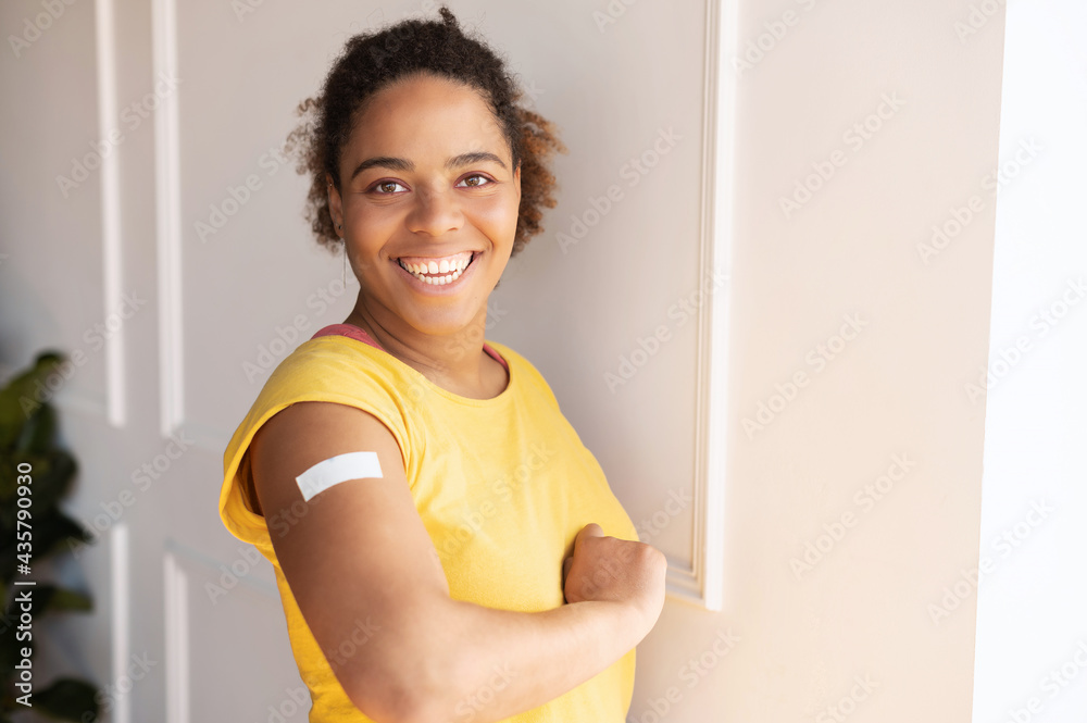 Cheerful vaccinated African-American woman showing arm with medical patch and laughs, black female getting vaccine dose against covid, plaster on her shoulder, isolated on white. Healthcare concept