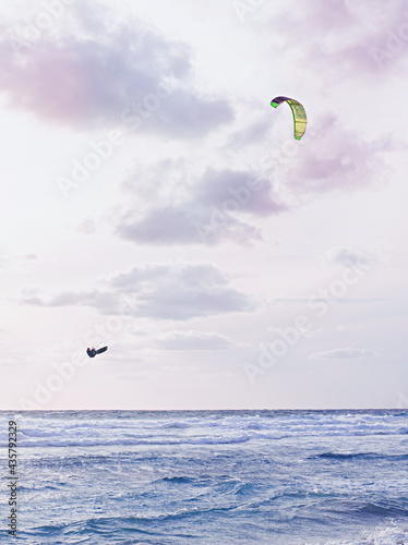 kitesurfers in the sky in the evening duck over the blue water of mediterranean sea