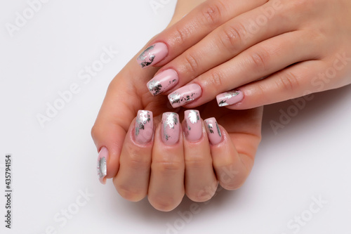 Holiday nails. Exclusive. Gel nude  beige nails with silver foil on long square nails close-up on a white background.