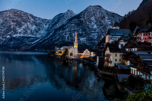 VIew of beautiful Hallstatt lake and famous church during late evening after sunset in early spring with mountain ranges