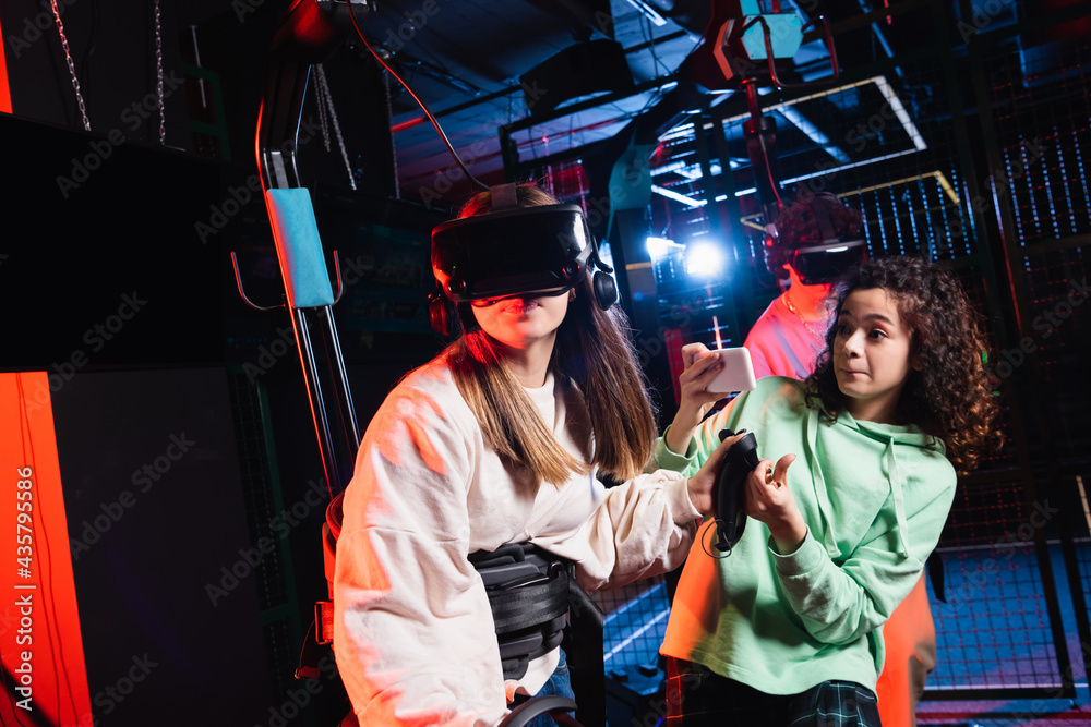 Obraz premium african american teenage girl taking photo of friend gaming in vr headset