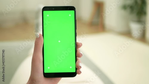 Woman lays on sofa and holds smartphone with green screen. Woman holds black smartphone with green screen. Digital device with chroma key background.