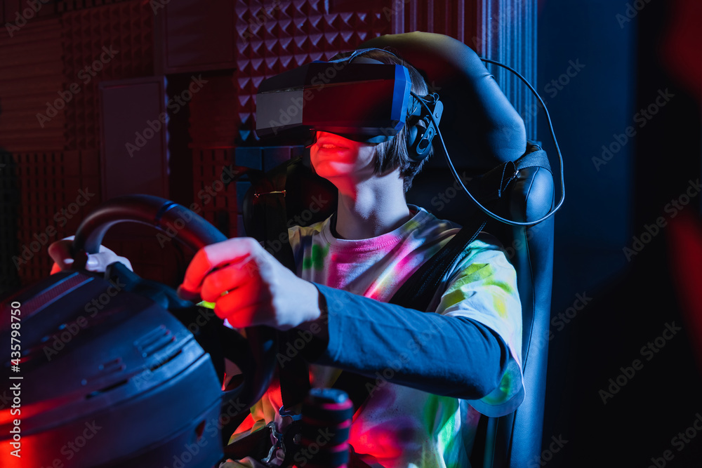 happy teenage boy holding steering wheel while gaming on car simulator