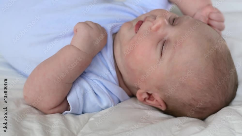 Newborn baby portrait. Close up face infant baby laying on a soft blanket. One month child waking up, opening eyes, yawning and smiling. Hungry little child sucking fingers. Infancy concept. Newborn baby portrait. Close up face infant baby laying on a soft blanket. One month child waking up, opening eyes, yawning and smiling. Hungry little child sucking fingers. Infancy concept.