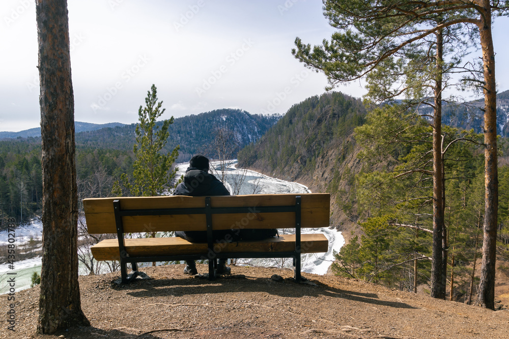 Back view of a young guy sitting on a bench over the river canyon Back view of a young guy sitting on a bench over the river canyon