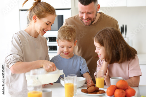 Young happy family with two cute little kids having breakfast together in kitchen and smiling