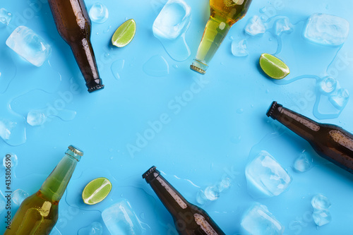 Full transparent and dark glass bottles with beer, without labels, with flowing drops, lie with of ice and lime
