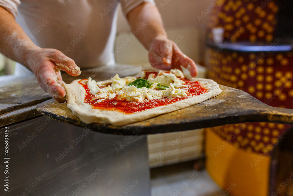 Pizza margherita napoletana con sugo di pomodoro, mozzarella di bufala e basilico mentre viene stesa su una pala di legno da forno