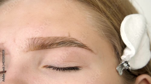 Gloved master shaping shape of the eyebrow with a cosmetic brush close-up. Permanent makeup for eyebrows. Eyebrow lamination and styling. Long shot full hd