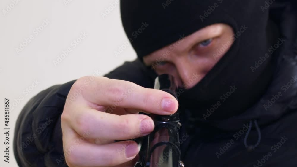 A police sniper in a black blaclava with blue eyes makes corrections on the telescopic sight of a sniper rifle, sends the chamber into the chamber by twitching the bolt. Release of hostages. Close-up. A police sniper in a black blaclava with blue eyes makes corrections on the telescopic sight of a sniper rifle, sends the chamber into the chamber by twitching the bolt. Release of hostages. Close-up.