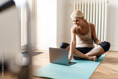 Blonde mature woman using laptop during yoga practice at home