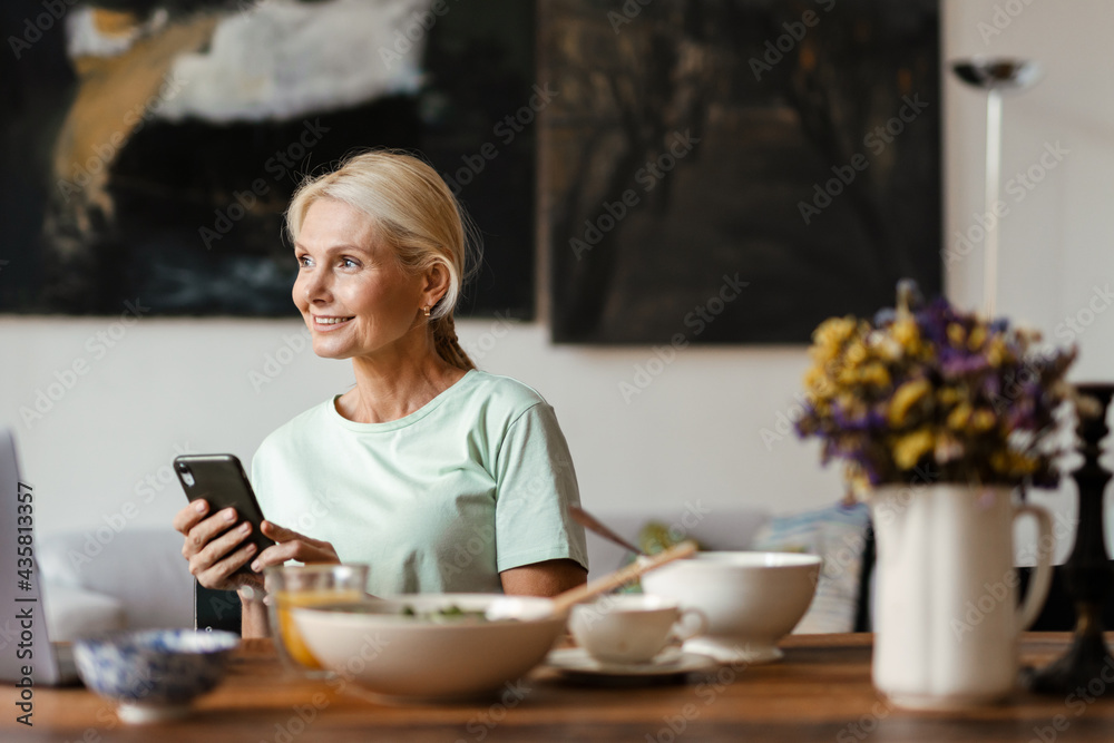 Blonde mature woman using laptop and cellphone while having lunch Blonde mature woman using laptop and cellphone while having lunch