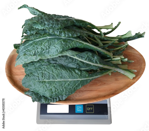 Kale leaves are in a wooden tray. On weight scales isolate whit backgruond.