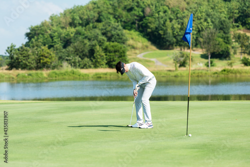 Golfer man playing golf aiming shot for putting ball on the hole with club on green course. Professional people hobby in holiday and vacations in sunny morning day on club golf