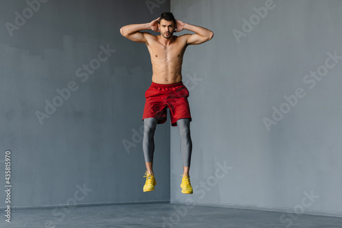 Young shirtless sportsman jumping while working out indoors
