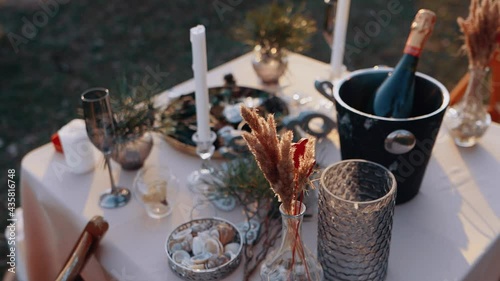 The close frame of a decor. Romantic dinner in nature, table with flowers, candles, cutlery and champagne. The beauty of nature in the evening