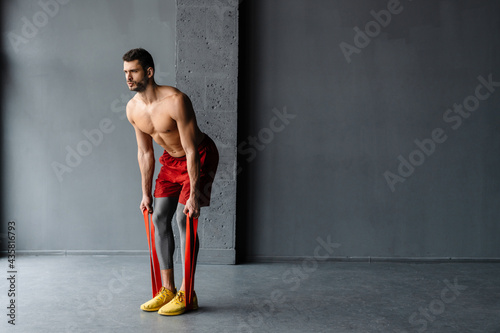 Young shirtless sportsman doing exercise with expander stretch tape © Drobot Dean