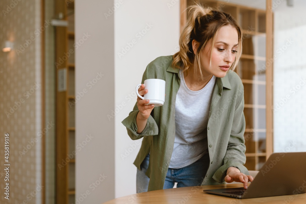 Young white woman drinking coffee and using laptop at home Young white woman drinking coffee and using laptop at home
