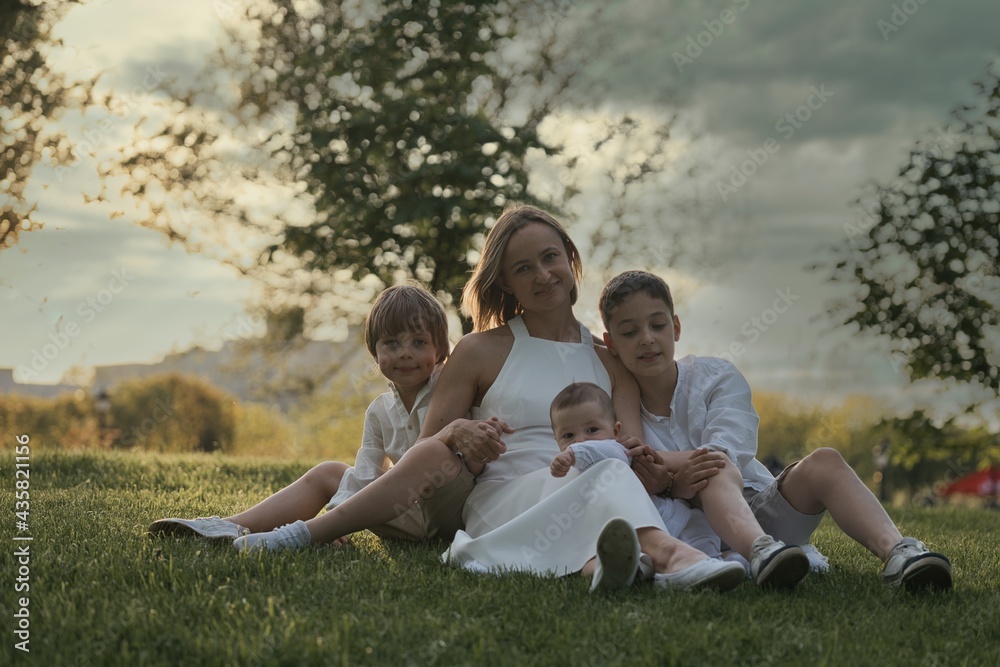 Mother and three children hugging. Happy family sitting outdoor: woman and two brother kids boys and cute little toddler boy Mother and three children hugging. Happy family sitting outdoor: woman and two brother kids boys and cute little toddler boy
