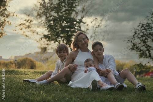 Mother and three children hugging. Happy family sitting outdoor: woman and two brother kids boys and cute little toddler boy