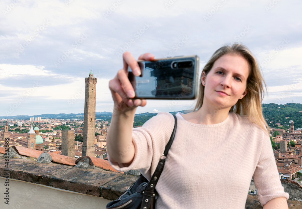 Young beautiful blonde woman tourist taking selfie portrait with  two towers in the background. Bologna, Italy.